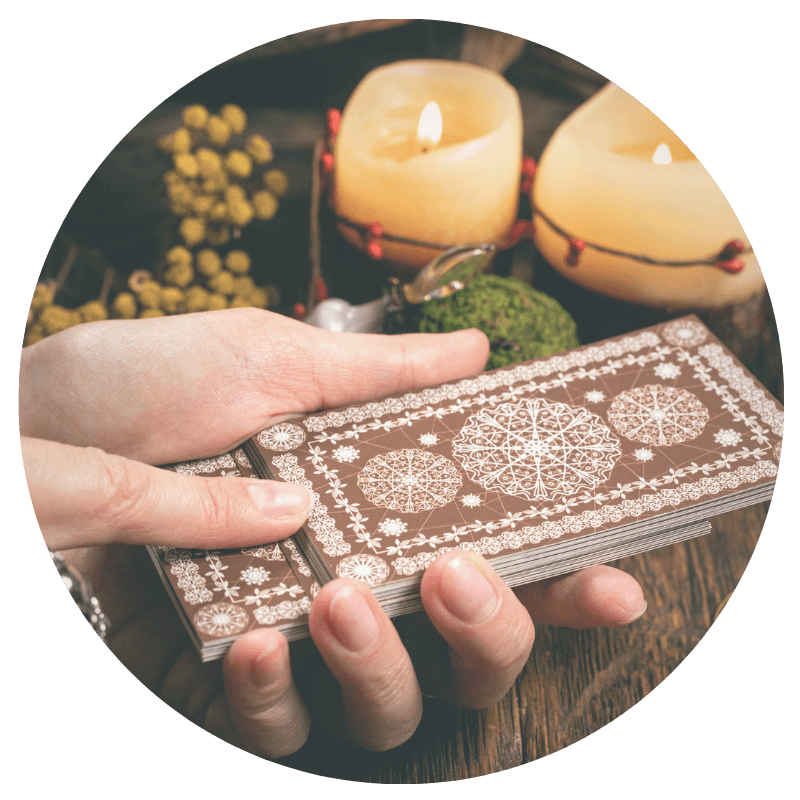 white person's hand holding a deck of brown tarot cards with candles in the background