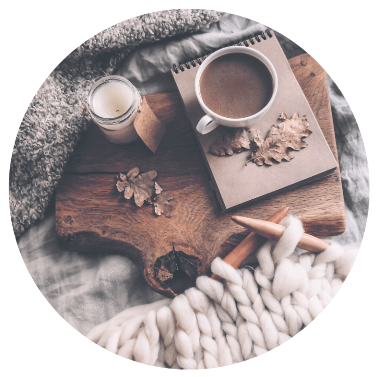 candle, hot chocolate, notepad and blankets on top of a bed